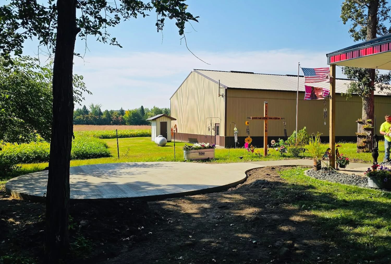 Circular concrete patio connected to a long curved walkway beside a barn
